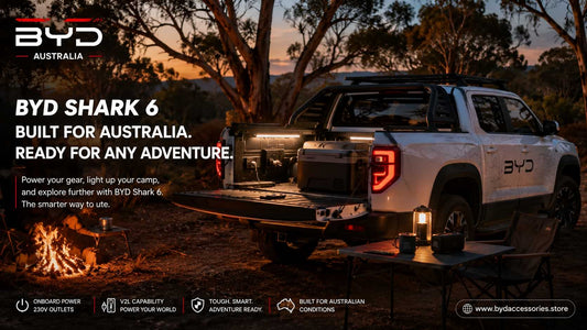White BYD Shark 6 ute at an Australian bush campsite at dusk with LED lighting, camp fridge, tailgate setup, and outdoor camping gear.